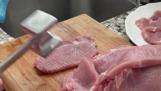 Tenderizing pork with meat mallet tool - using  meat tenderizer meat pounder to prepare slabs of pork and seasoning with salt for por schnitzels recipe at home in kitchen slow motion slo-mo
