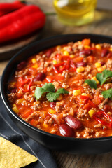 Bowl with tasty chili con carne on wooden table, closeup