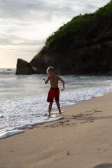 Fototapeta na wymiar A child on the beach plays in the waves of the ocean. Boy on the ocean, happy childhood. tropical life.