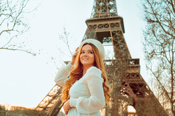 A girl against the backdrop of the Eiffel Tower in Paris in a beret and a dress with curled hair, a...