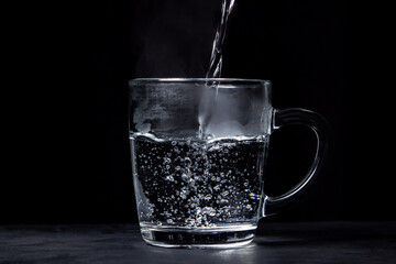 Boiling water is poured into a glass on a black background. Hot drinking water