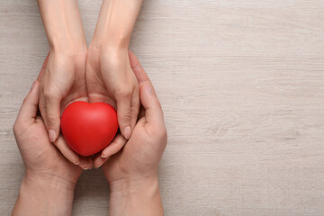 People holding red decorative heart on wooden background, top view and space for text. Cardiology concept