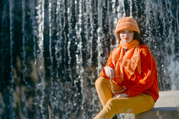 autumn portrait of a girl in a hat and orange sweater. woman sitting on the river bank.