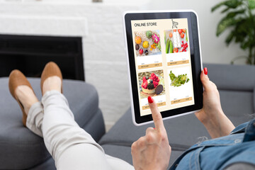 Back view of woman doing shopping online on website with digital tablet at home. Top view of lady on relaxing sofa. Rear view of girl hand touching screen while selecting product on e-commerce portal