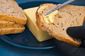 chef in gloves spreads butter with a knife on a slice of bread.
