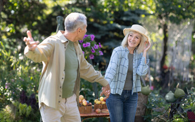Happy loving senior couple holding hands and walking in their garden on warm spring day, enjoying...