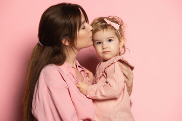 Kiss. Portrait of young woman and little girl, mother and daughter isolated on pink studio background. Mother's Day celebration. Concept of family, childhood, motherhood