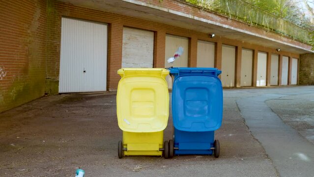 Trashes Falling Into Blue And Yellow Colored Garbage Bins. Ukrainian Flag Colored Garbage Bins Receiving The World's Waste, Including Russia's Aggression. static