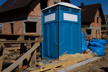 Portable mobile toilet for workers at the construction site of a new single-family house. Unfinished stand-alone home under construction, made of hollow blocks or bricks.