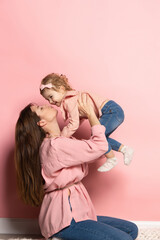 Portrait of young woman and little girl, mother and daughter isolated on pink studio background....