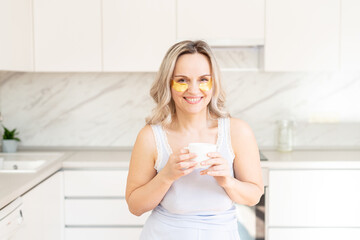 Middle age woman in pajama at kitchen with cosmetic collagen patches under eyes. Facial care. Skin...