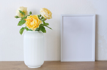 Square wooden frame mockup on a vintage bench, table. Modern white ceramic vase with yellow roses. White wall background. Scandinavian interior.