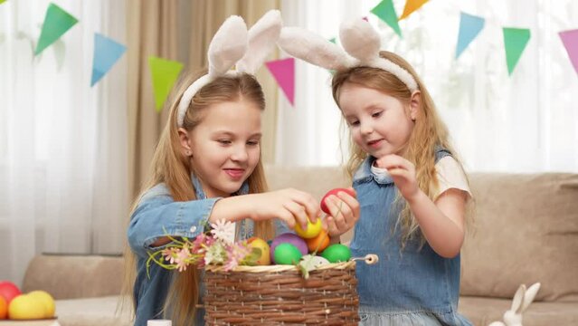 a happy little girls with rabbit ears put painted eggs in a basket.