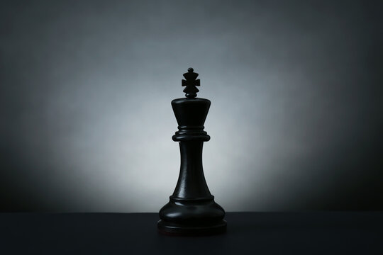 Black king on dark table against light background. Chess piece