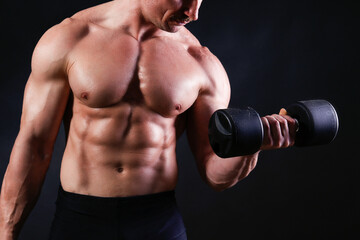 Fototapeta na wymiar Professional bodybuilder performing exercise with dumbbells over isolated black background. Studio shot of a male fitness model pumping iron. Close up, copy space.