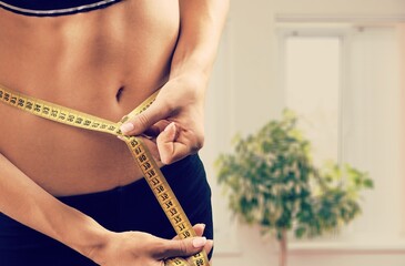 Portrait of cheerful young lady in sportswear measuring waist with tape, feeling happy