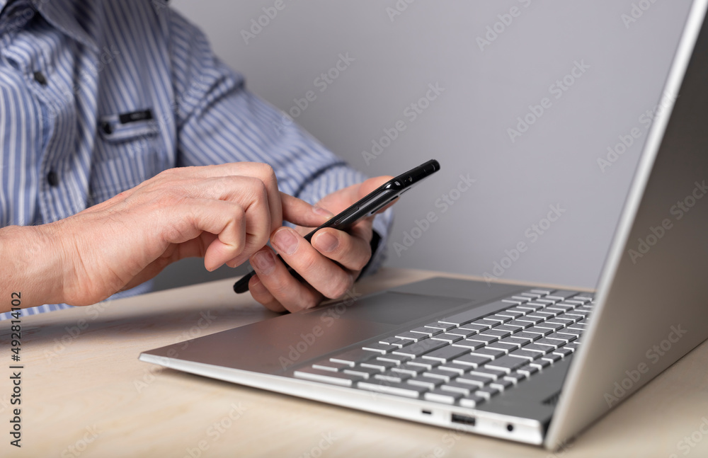 Poster man hands closeup holding phone while sitting at table with laptop. using gadgets for work, educatio
