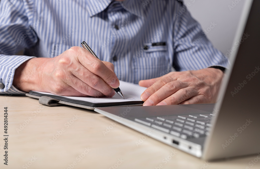 Poster Man sitting at table with laptop and writing with pen in diary. Hands closeup. Taking online courses, preparation for exams, planning concept. High quality photo