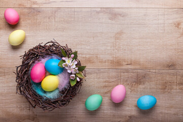 Nest with colorful Easter eggs and apple blossom on a wooden background. Easter concept with copy space, top view. Background, postcard with Easter decorations.