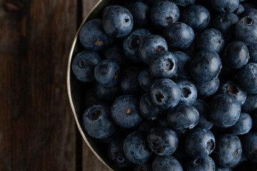 Bowl of fresh blueberries on rustic wooden table with copy space.