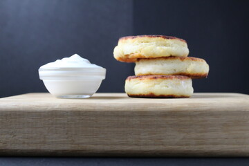 breakfast cottage cheese pancakes cheesecakes on a wooden tray with white sour cream sauce. Russian healthy breakfast dish cottage cheese healthy food
