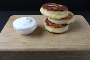 breakfast cottage cheese pancakes cheesecakes on a wooden tray with white sour cream sauce. Russian healthy breakfast dish cottage cheese healthy food