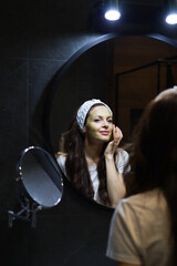 Fototapeta na wymiar Girl taking care of oily complexion by using green clay mask. Woman in headband