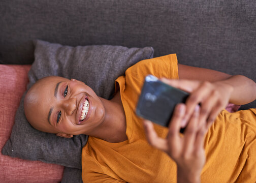 An Overhead View Of A Young Woman Lying On The Couch On Her Phone