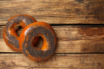 Delicious fresh bagels with poppy seeds on wooden table, flat lay. Space for text