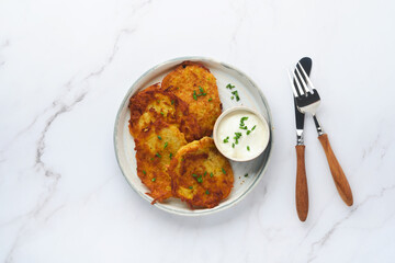 Potato pancakes. Fried homemade potato pancakes or latkes with cream and green onions in rustic plate on white marble table background. Rustic style. Healthy food. Top view.