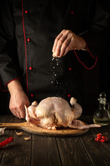 Professional chef preparing raw chicken in the kitchen. The cook adds salt to the chicken before roasting. Asian cuisine.