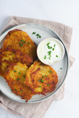 Potato pancakes. Fried homemade potato pancakes or latkes with cream and green onions in rustic plate on white marble table background. Rustic style. Healthy food. Top view.