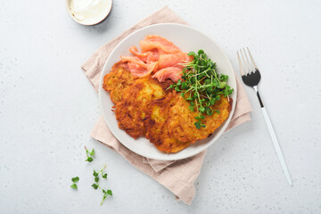 Potato pancakes. Fried homemade potato pancakes or latkes with cream, green onions, microgreens, red salmon and sauce in rustic plate on white table background. Rustic style. Healthy food. Top view.