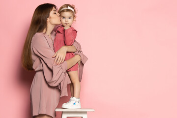 Emotional woman and little girl, caring mother and daughter isolated on pink studio background....