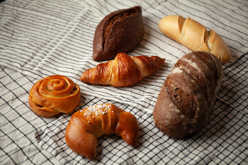 White and black bread, cereal rolls, crispy baguette on a towel on the table.