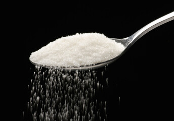 White sugar teaspoon on black background.