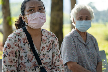 Asian elderly woman and daughter in social distancing sitting bench and wearing face mask for...