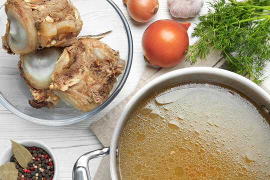 Delicious homemade bone broth and ingredients on white wooden table, flat lay