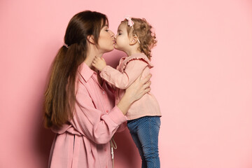 Kiss. Happy woman and little girl, caring mother and daughter isolated on pink studio background. Mother's Day celebration. Concept of family, childhood, motherhood