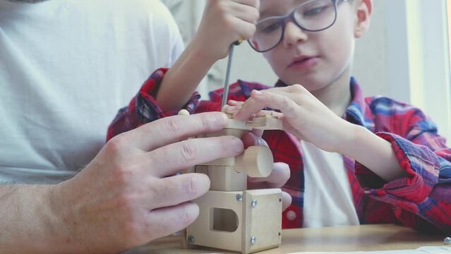 Happy father's day and childhood concept. Close-up of a father and a boy son in glasses work with hand tools, using a screwdriver, assembling a wooden house constructor at the table