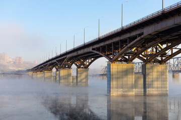 Bridge hidden in the fog at frost winter day in early morning. Urban landscape with Yenisei river at Krasnoyarsk, Russia