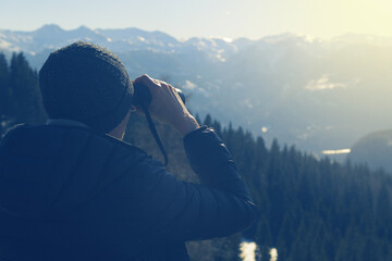 Close-up of a man with binoculars watching beautiful Alpine landscape before sunset