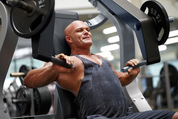Building up his muscle mass. Shot of a male bodybuilder using exercise equipment at the gym.