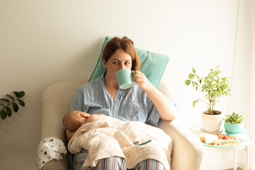 Woman drink tea or coffee during process of breastfeeding of newborn baby