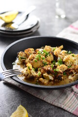 Healthy grilled cauliflower recipe with lemon, garlic and green onions suitable for diet, backlight, black plate, gray background