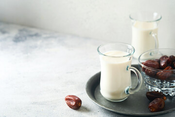 Ramadan Kareem food and drinks. Plate of dates, glass of milk and date palm branch on light grey background. Righteous Muslim Lifestyle. Place for text. Selective focus.