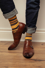 Studio photo of a pair of men's feet wearing a pair of yellow striped socks, brown leather shoes,...