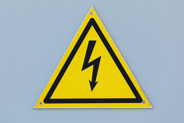 Black caution or warning electrical triangle sign or table on yellow background on the beige painted steel wall