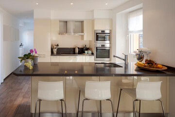 Light modern kitchen with large dark island with stools. Bright window illuminates the scene