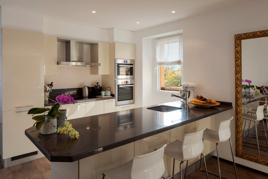 Light modern kitchen with large dark island with stools. Bright window illuminates the scene